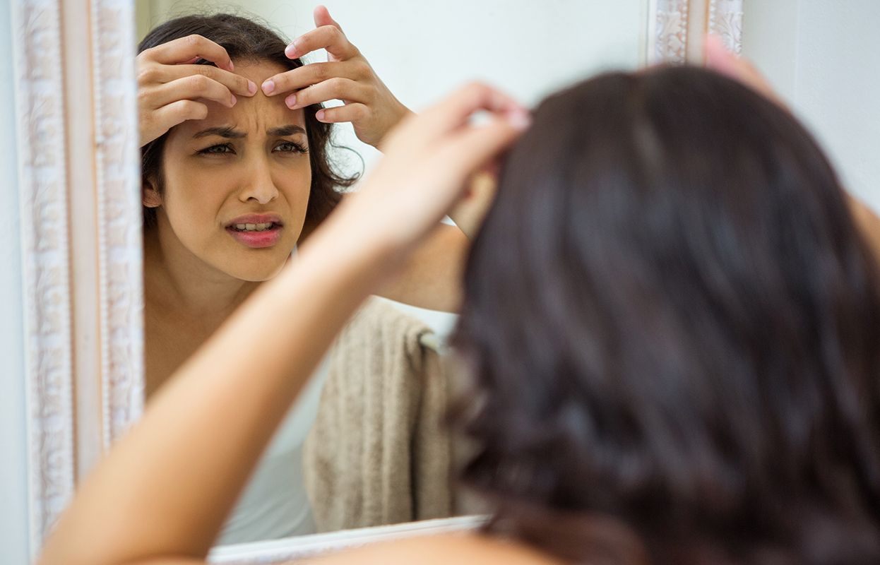 Close-up of a woman looking at her hair in the mirror with an unhappy expression